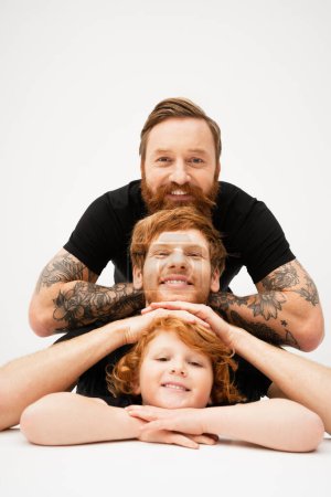family portrait of redhead men and cheerful boy posing on light grey background