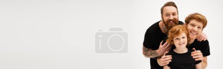 Photo for Family portrait of redhead boy with father and tattooed grandpa embracing isolated on grey, banner - Royalty Free Image