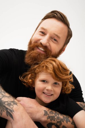 family portrait of red haired boy with bearded tattooed grandpa smiling at camera isolated on grey