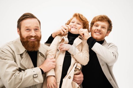 happy bearded man looking at camera near redhead son and grandson having fun isolated on grey