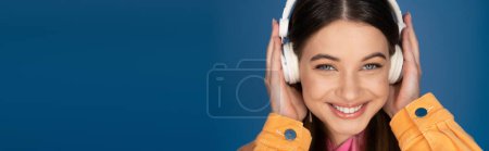 Foto de Positive teen girl in wireless headphones looking at camera isolated on blue, banner - Imagen libre de derechos