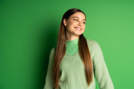 Smiling teenager in jumper looking away on green background 