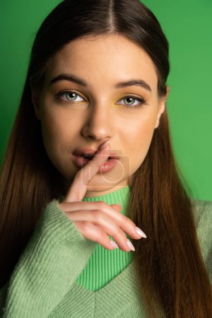 Portrait of teen girl showing secret gesture on green background 