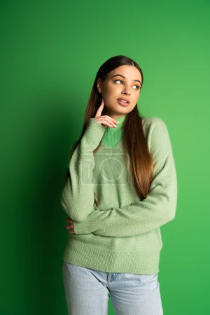 Brunette teen girl in jumper looking away on green background 