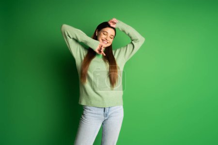 Happy teen girl in jumper and jeans standing on green background 