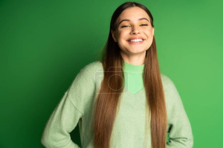 Pleased teen girl in jumper looking at camera on green background 