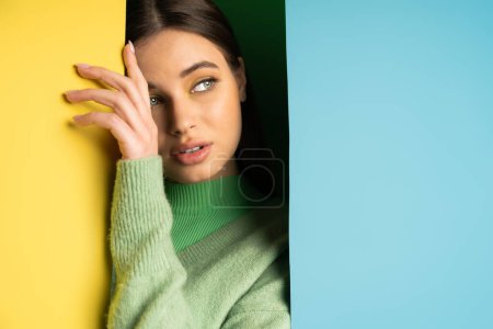 Brunette teenager in jumper touching colorful background 