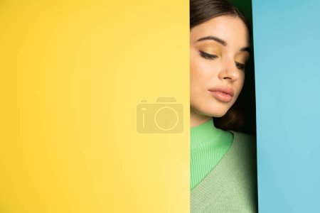 Teenager in jumper standing near blue and yellow background 
