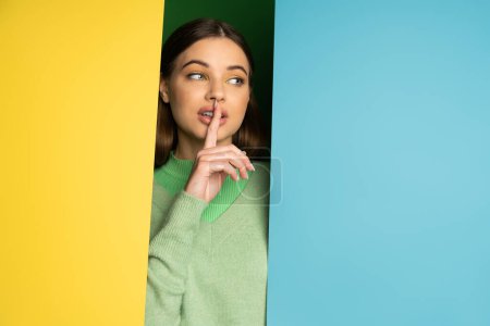 Pretty teen girl showing shh gesture on colorful background 
