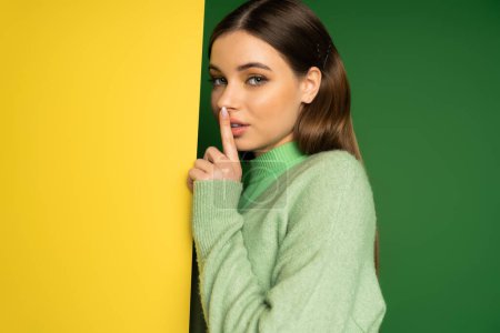 Brunette teenager in jumper showing quiet sign on colorful background 