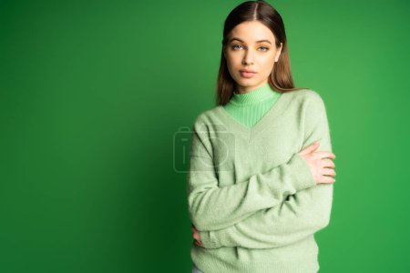 Brunette teen girl in cozy jumper looking at camera on green background 