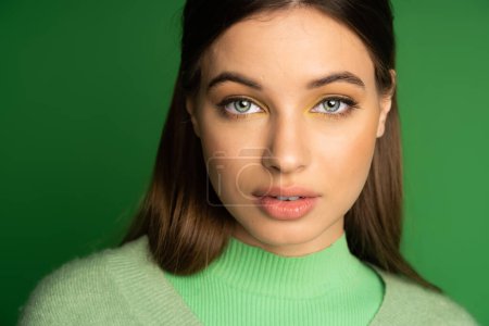 Portrait of teen girl with makeup looking at camera isolated on green 