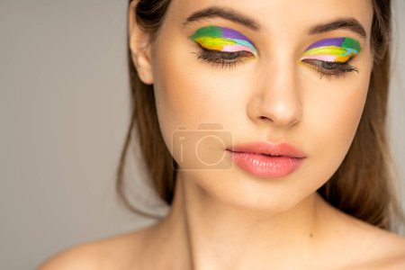 Photo for Teenage girl with colorful makeup and naked shoulder looking down isolated on grey - Royalty Free Image