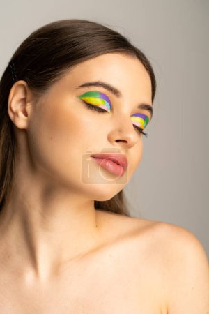 Brunette teenage girl with multicolored eyeshadows posing isolated on grey 