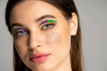 Close up view of teen girl with colorful makeup looking at camera isolated on grey 
