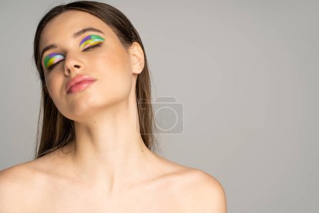 Teen girl with naked shoulders and colorful visage closing eyes isolated on grey 