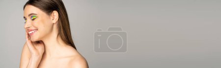 Photo for Pretty teen girl with multicolored visage and naked shoulders touching face isolated on grey, banner - Royalty Free Image
