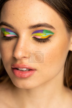 Portrait of freckled teenager with colorful eyeshadows isolated on grey 