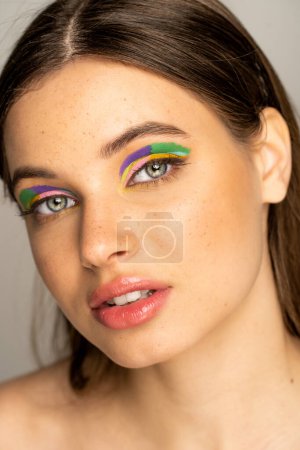 Photo for Brunette teen girl with multicolored makeup and freckles looking at camera isolated on grey - Royalty Free Image