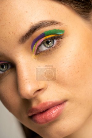 Photo for Cropped view of freckled teen girl with colorful eyeshadows isolated on grey - Royalty Free Image