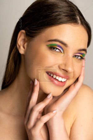 Photo for Brunette teenager with colorful eyeshadows looking at camera isolated on grey - Royalty Free Image