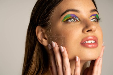 Photo for Teenage model with colorful visage touching face and looking away isolated on grey - Royalty Free Image