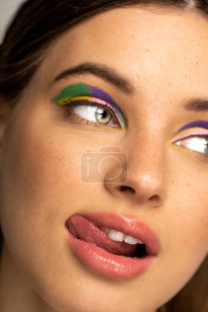 Téléchargez les photos : Cropped view of teen model with multicolored makeup sticking out tongue - en image libre de droit
