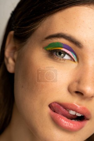 close up view of teenager with colorful visage sticking out tongue and looking at camera 