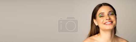 Photo for Teen girl with naked shoulders and multicolored makeup looking at camera isolated on grey, banner - Royalty Free Image