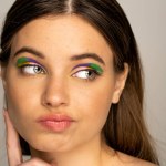 Pensive teenage model with colorful makeup looking away isolated on grey