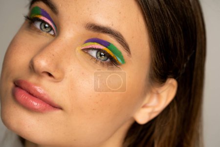 Téléchargez les photos : Portrait of freckled teenager with creative makeup looking at camera isolated on grey - en image libre de droit