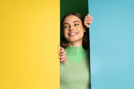Smiling teen model in soft jumper looking away near colorful background 