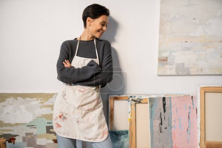 Cheerful artist looking at drawings near wall in workshop 