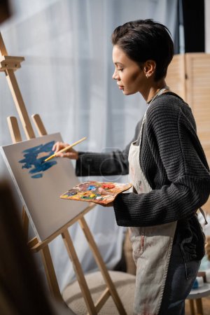 Foto de Side view of brunette artist painting on canvas in studio - Imagen libre de derechos