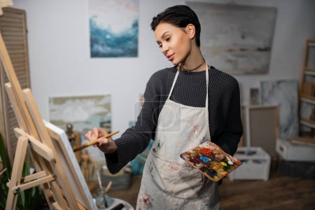 Brunette short haired artist painting on canvas in studio 
