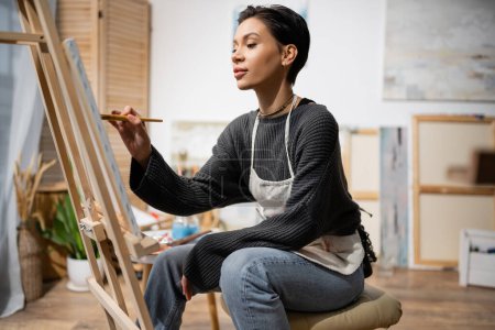 Téléchargez les photos : Short haired artist sitting and painting on canvas in studio - en image libre de droit