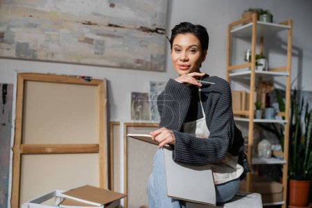 Young artist holding pencil and sketchbook and looking at camera in workshop  Mouse Pad 634324828