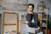 Young artist holding pencil and sketchbook and looking at camera in workshop  mug #634324828