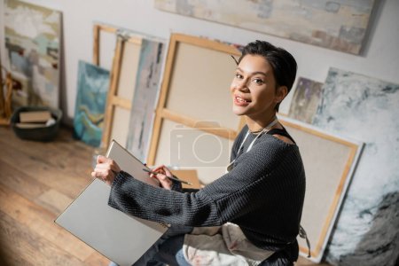 Young short haired artist holding pencil and sketchbook in studio 