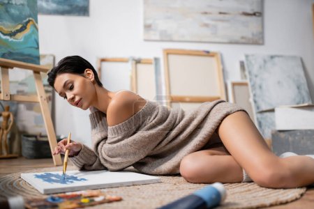 Téléchargez les photos : Sexy short haired artist painting on canvas on floor in blurred workshop - en image libre de droit