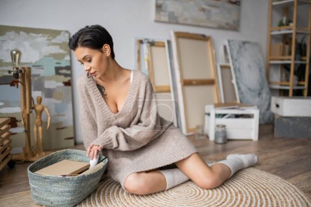 Sexy artist in sweater looking at sketchbooks in basket in workshop  tote bag #634326370