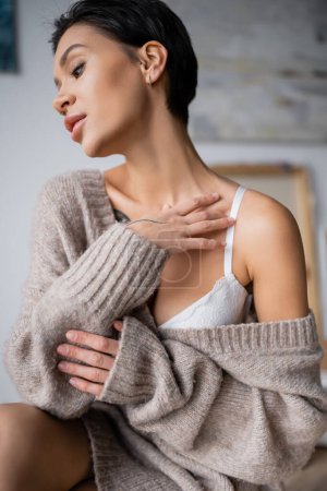 Photo for Sexy brunette artist in sweater touching chest in studio - Royalty Free Image