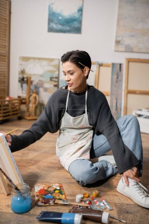 Young artist in messy apron painting on canvas in studio 