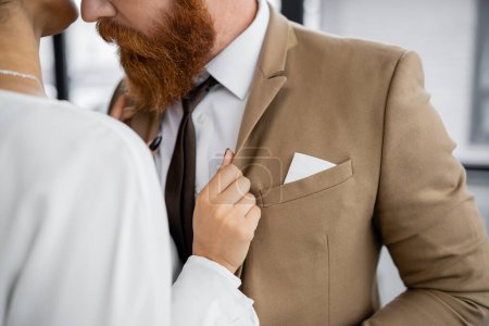 cropped view of african american woman adjusting blazer of bearded businessman in formal wear 