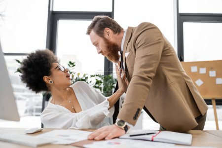 shocked african american woman pushing away businessman in office 