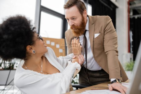 shocked african american woman pushing away bearded businessman in office 