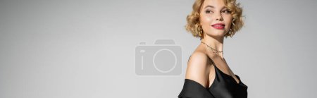 Photo for Joyful young woman in black slip dress looking away isolated on grey, banner - Royalty Free Image