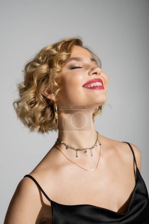 Photo for Portrait of joyful young woman with closed eyes smiling isolated on grey - Royalty Free Image
