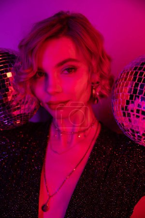 young woman with blonde hair near shiny disco balls on purple and pink 