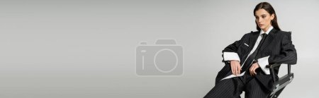 Téléchargez les photos : Pretty woman in white shirt and black striped suit sitting on chair isolated on grey, banner - en image libre de droit